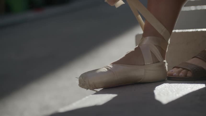A ballet dancer ties up her pointe shoes