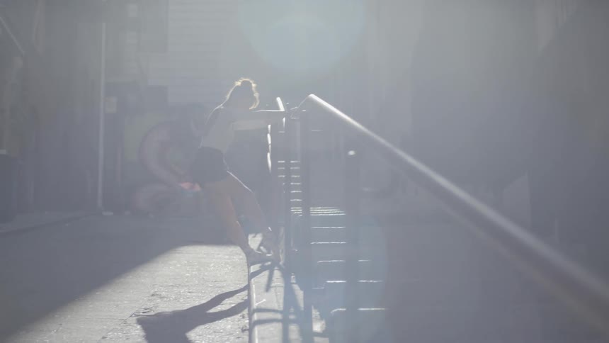A ballet dancer stretches her leg while holding onto a stair banister outdoors