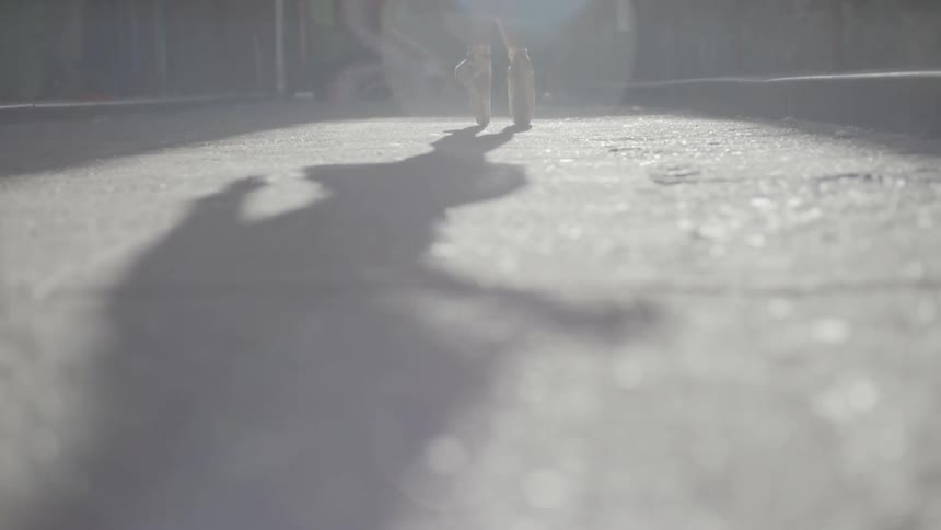 A ballet dancer dances outdoors in front of a fence