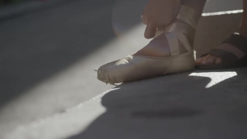 A woman is lacing up her ballet shoes