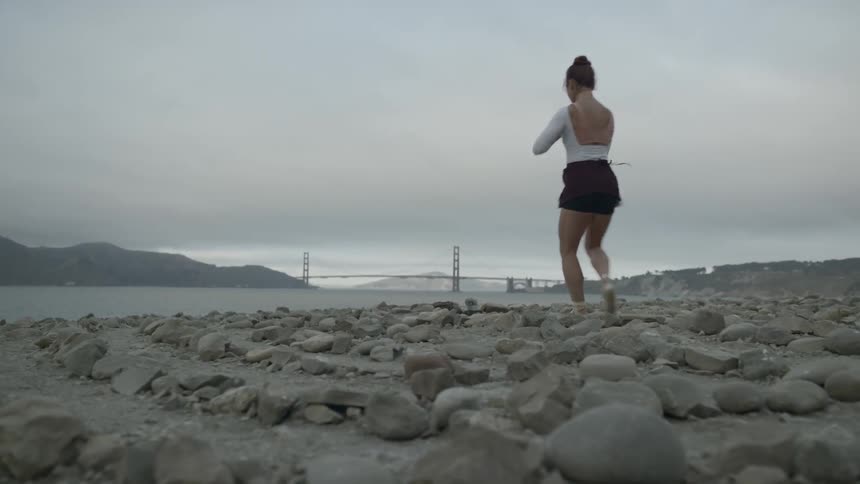 A dancing performing ballet moves on a rocky beach on a cloudy day