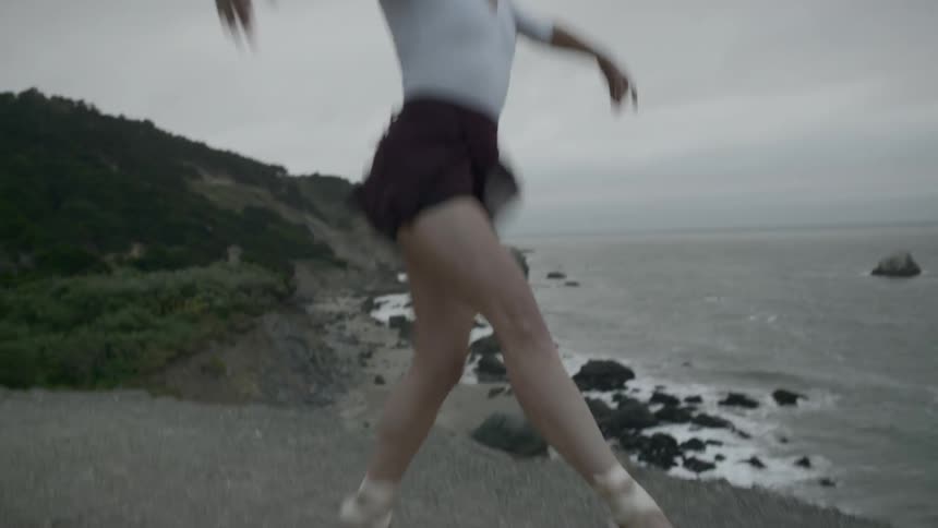 A ballet dancer dances outdoors near the water on gravel