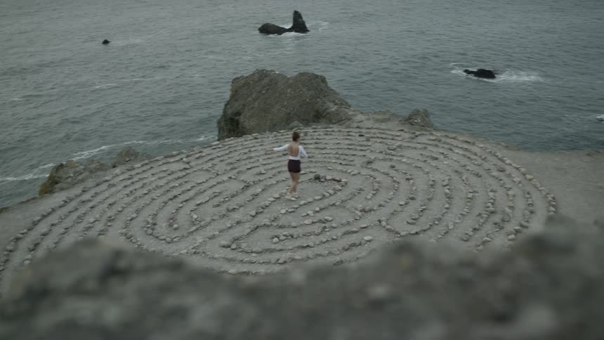 Woman dances in center of rock pattern on shore