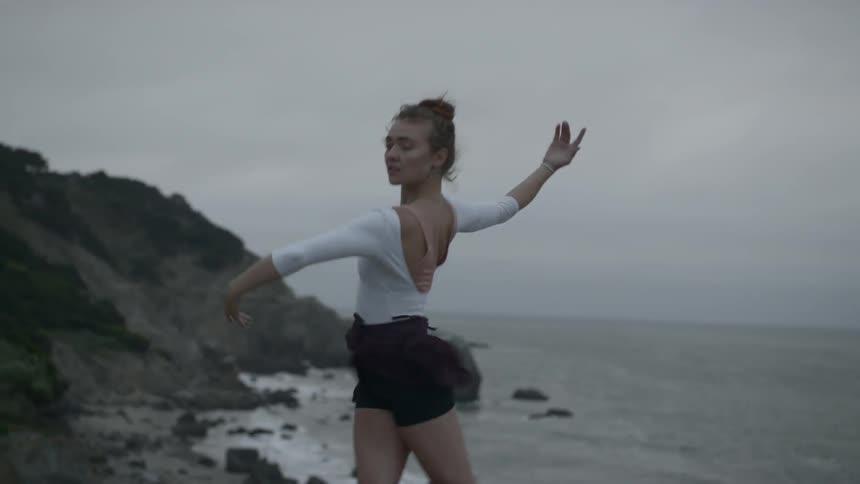 A young white woman dancing by the ocean on a gray and windy day