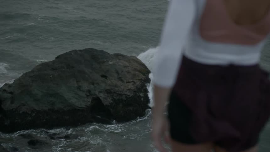 A young woman reaching towards the sky while standing on a cliff above the ocean