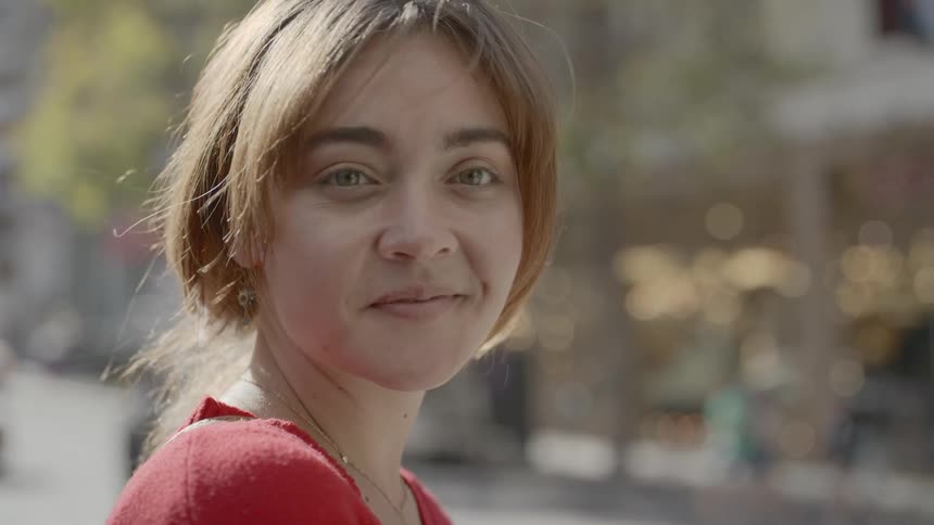 A woman smiles while posing in a busy pedestrian location in a city