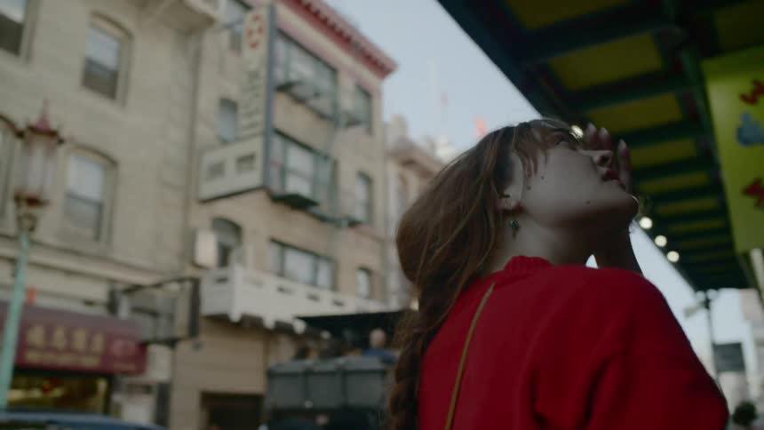 A young woman walks through an urban neighborhood displaying numerous signs for shops and stores