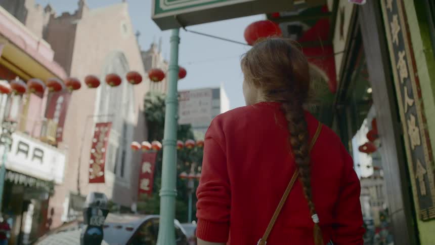 A woman walks through chinatown and looks up at paper lanterns decorating the street