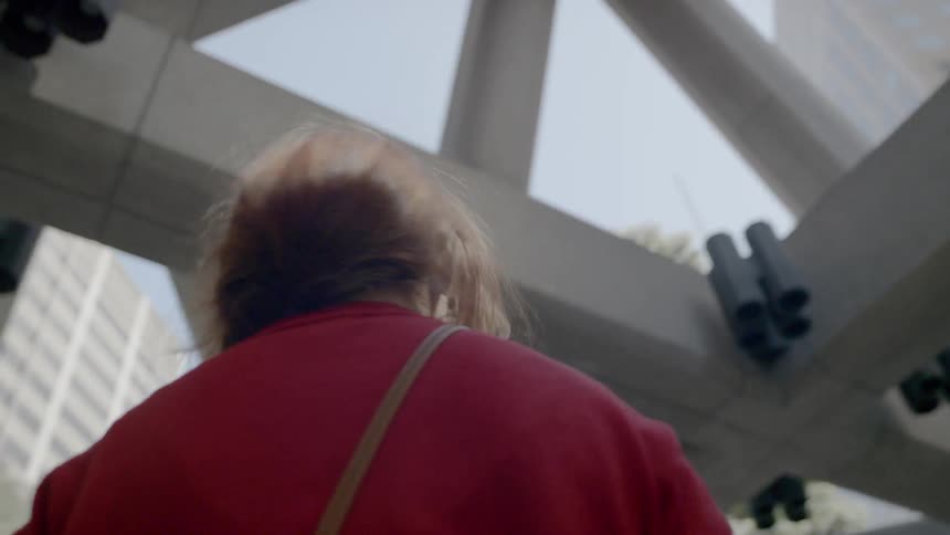 A woman holding her phone stands in an atrium and looks up at the surrounding buildings on a sunny day
