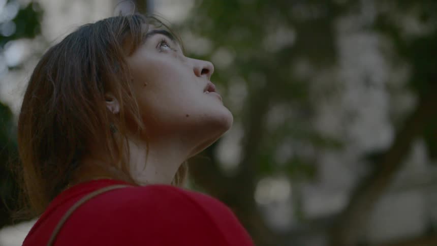 A young woman in red looking up at a tree