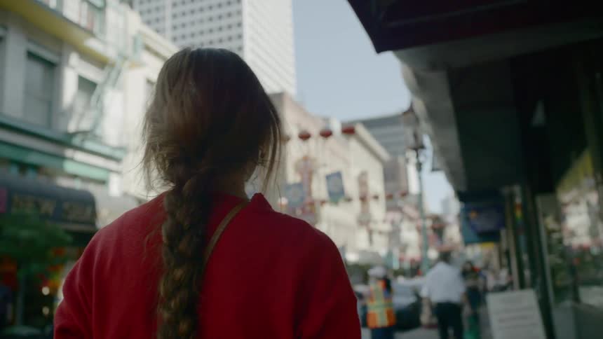 A woman walks down a city street decorated with chinese lanterns and full of traffic