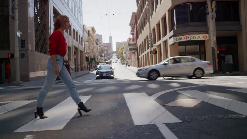 Woman wearing blue jeans and high heels crosses busy city street on a sunny afternoon