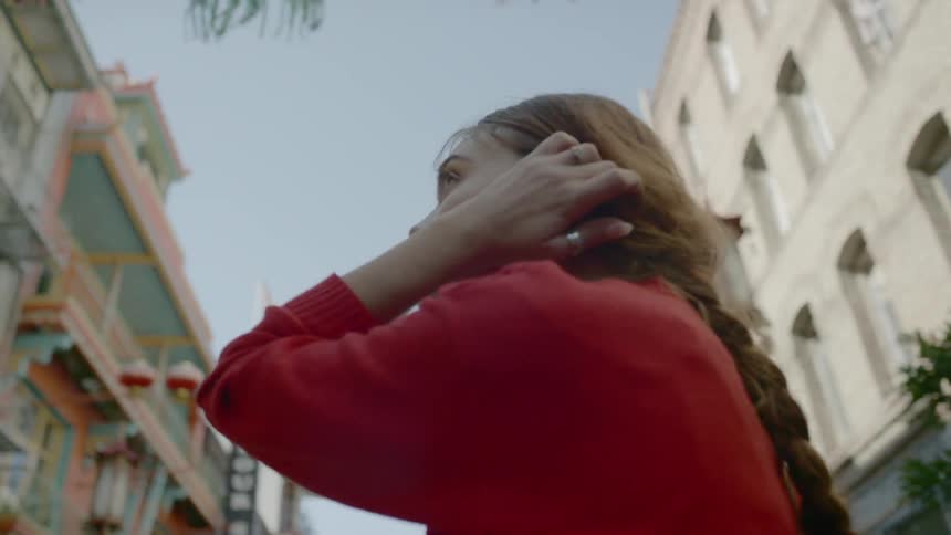 A young woman turns and looks at her surroundings as she stands in a neighborhood filled with many tall buildings