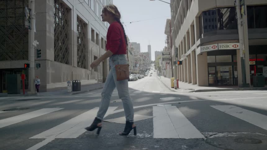 Blonde woman wearing a red sweater and high heels passes the pedestrian crossing in the city