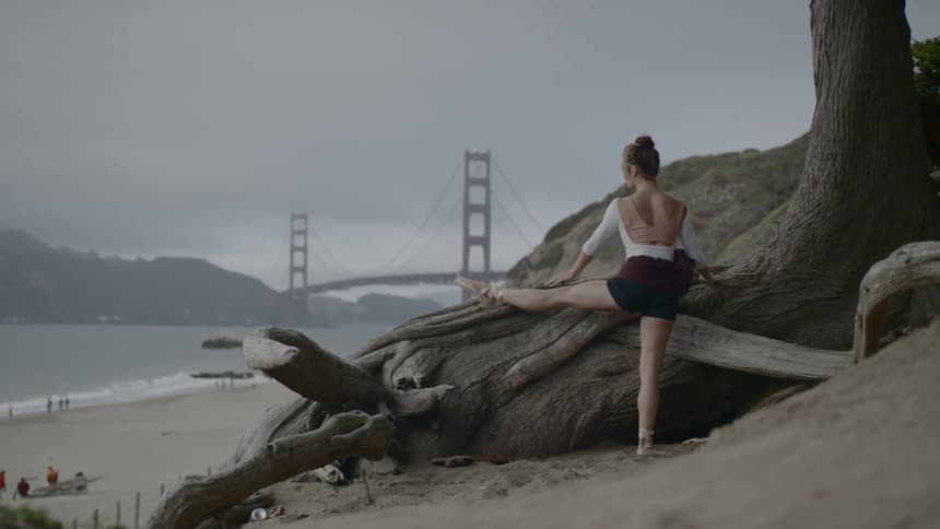 Woman wearing ballet attire stretching on a cliff near the beach