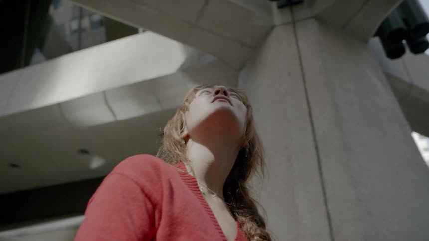 A woman stands under a patio outside a large building and looks up