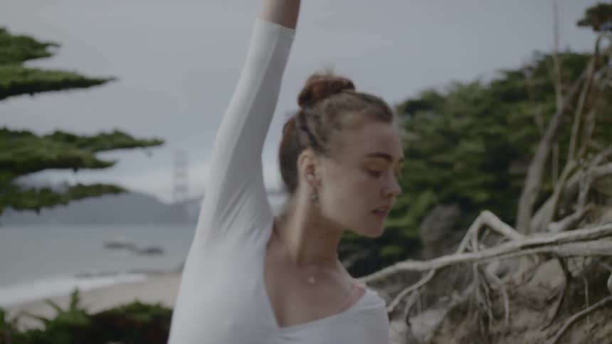 A woman dancing with the beach and a bridge in the background