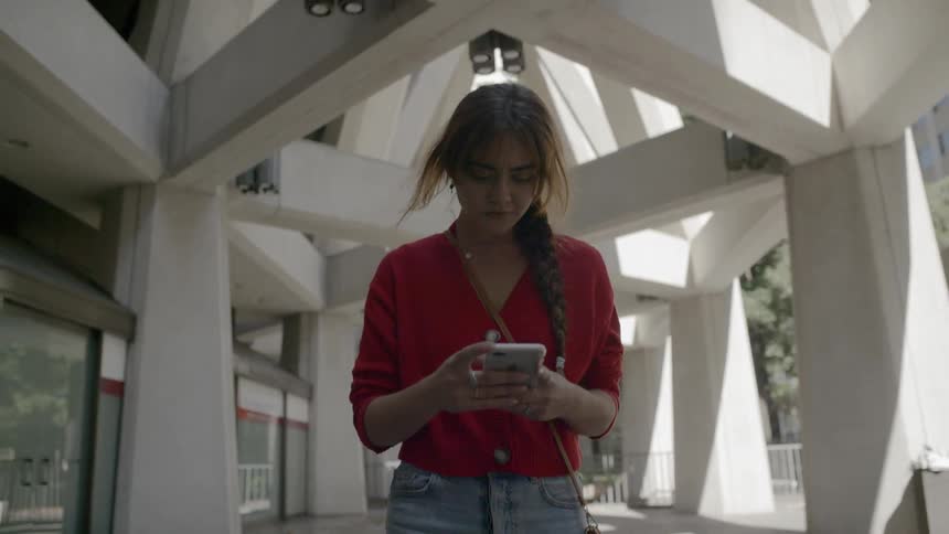 A young woman walks along the outside of a large building with unique architecture