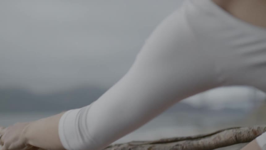 A female ballerina places her foot atop a fallen tree outdoors as she stretches her leg