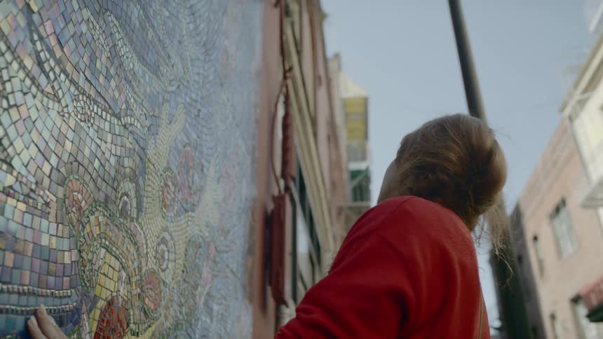Woman wearing a red sweater touches the wall mosaic in the street