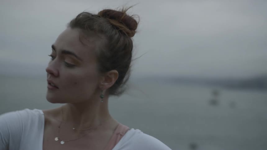 Ballerina dances on the hill next to the sea on a cloudy day