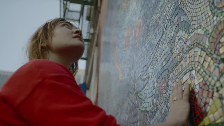 A woman running her hand along a wall covered in small colored tiles