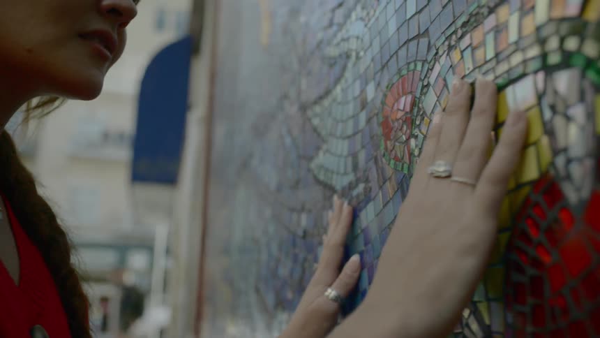 A woman runs her hands along a color mosaic outdoors