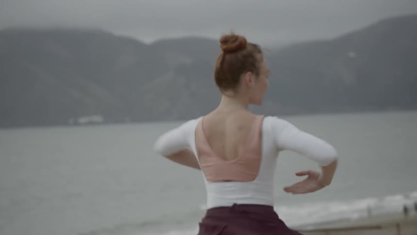 Ballerina moves rhythmically following a set sequence of steps on the hill by the seaside with the long distance view of golden gate bridge