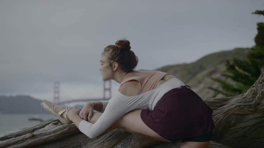 A woman with ballerina shoes stretching her leg on a log