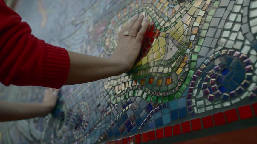 A woman running her hands along an artwork of colored stones