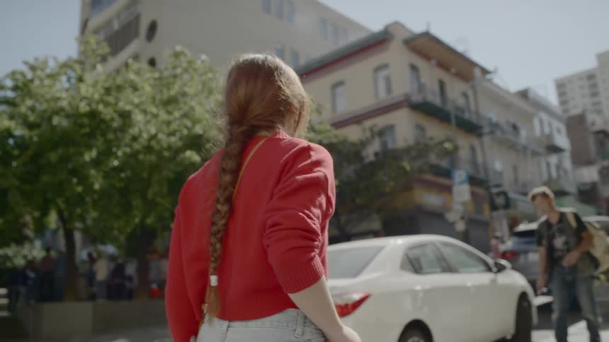 Woman wearing high heels and a red sweater walks down the street in the city