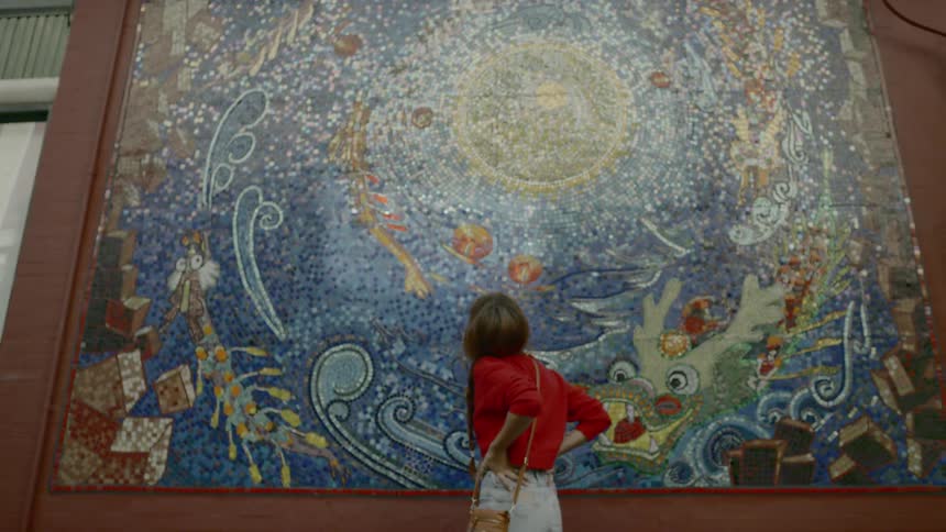 A woman stands and looks at a mosaic