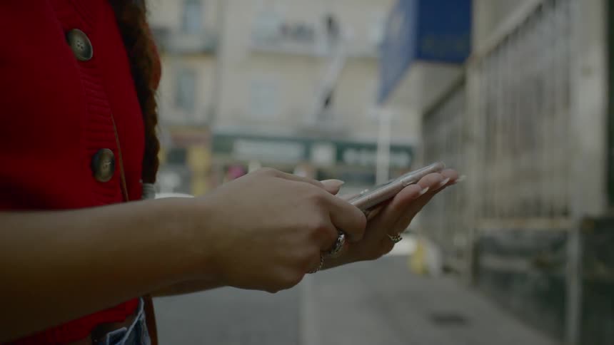 Woman wearing a red sweater uses tablet in the street