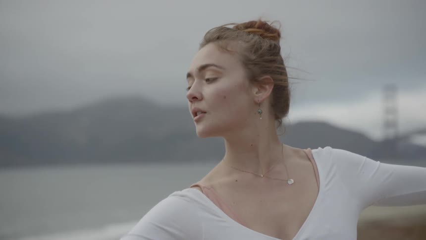 A young ballerina performs graceful dance moves outdoors at the coast with the golden gate bridge in the distance