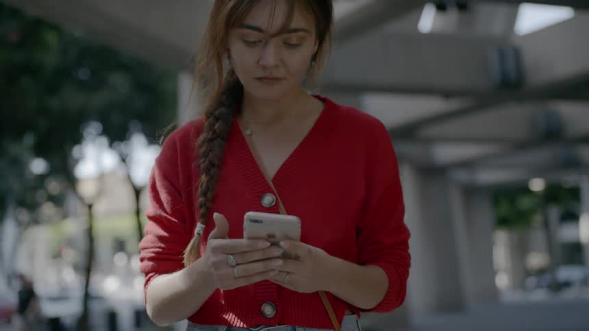 Blonde woman wearing a red sweater walks in the building while using a smartphone
