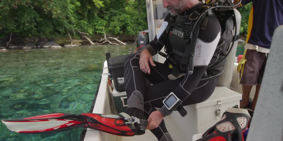 A man is fastening flippers on his feet while sitting on a boat