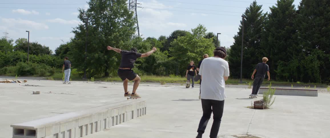 A group of young men at a skate park and ones does a jump onto a low wall