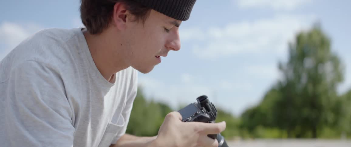 Photographer wearing a brown beanie hat take picture of people riding a skateboard outdoors