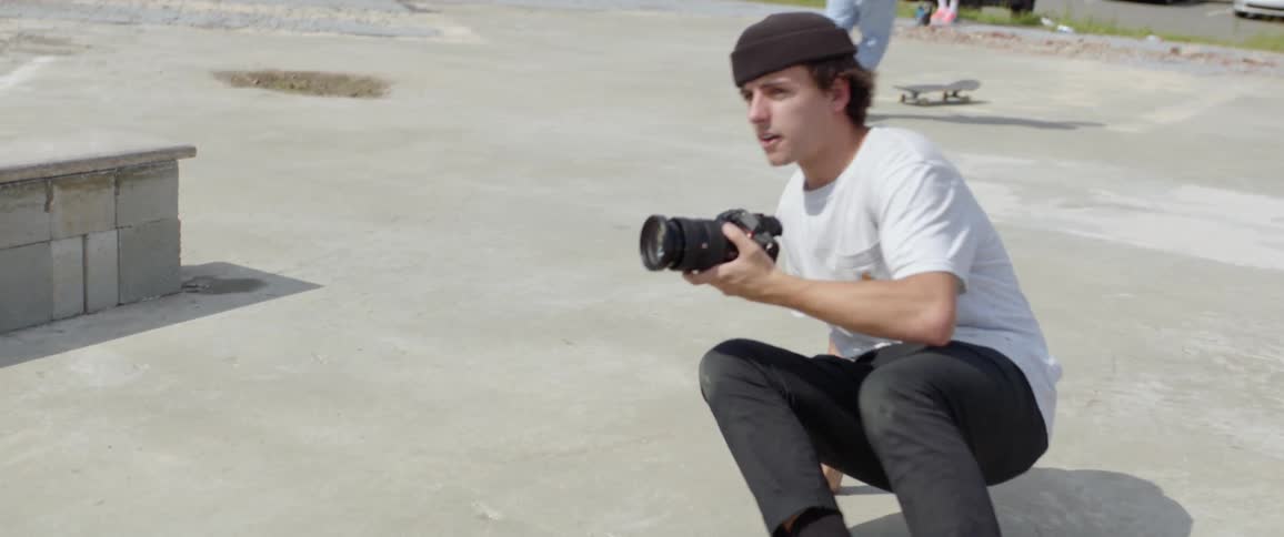 A photographer at a skate park gets down on the ground to get a shot