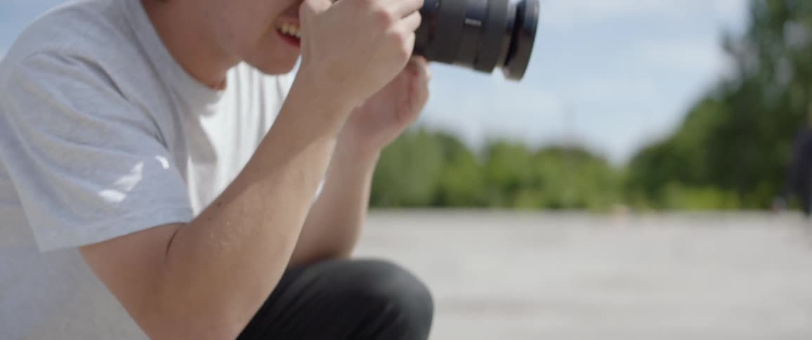 Male photographer wearing a brown beanie hat takes picture of people riding a skateboard outdoors