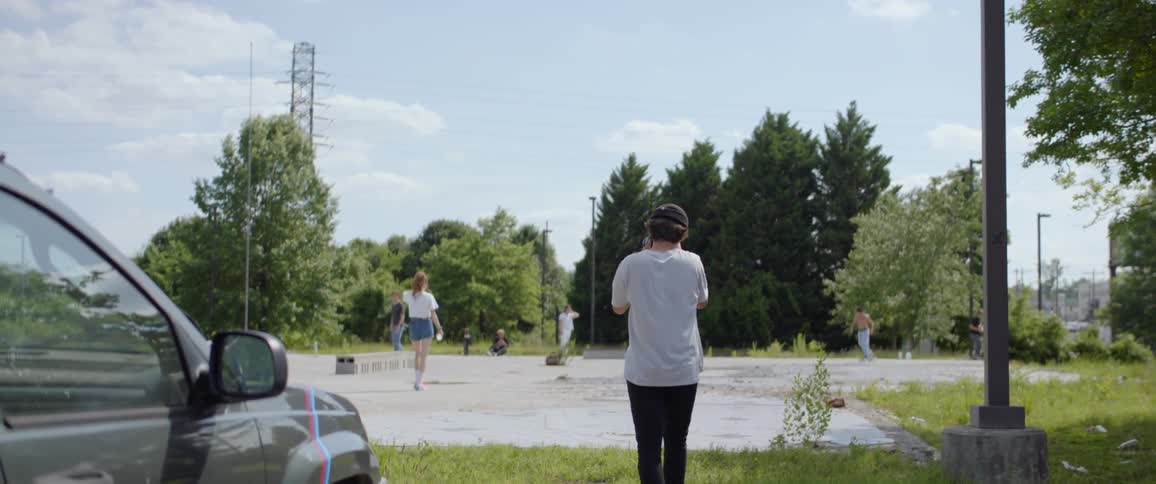 A small group of people gather in an empty concrete lot to skateboard