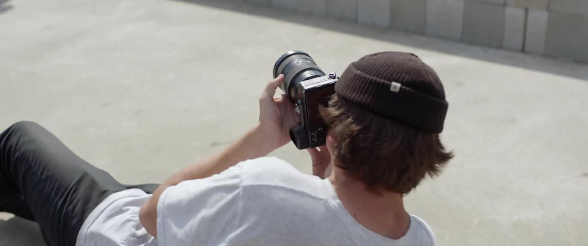 A young male photographer lays on the ground to get a good shot of a skateboarder performing a trick