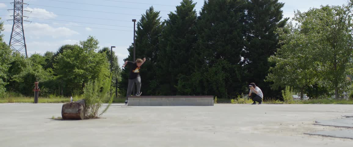 A young man rides a skateboard across a low wall in a park