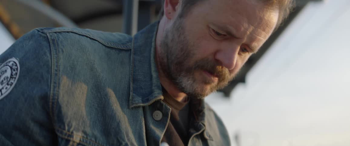 A middle aged white man wearing a jean jacket draws on a tablet
