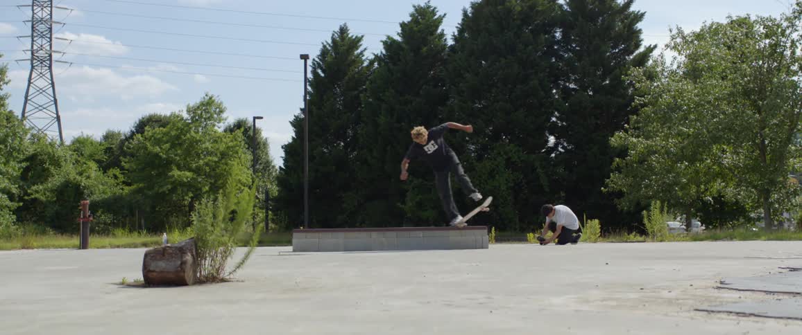 A young male skateboards across a low wall at a park