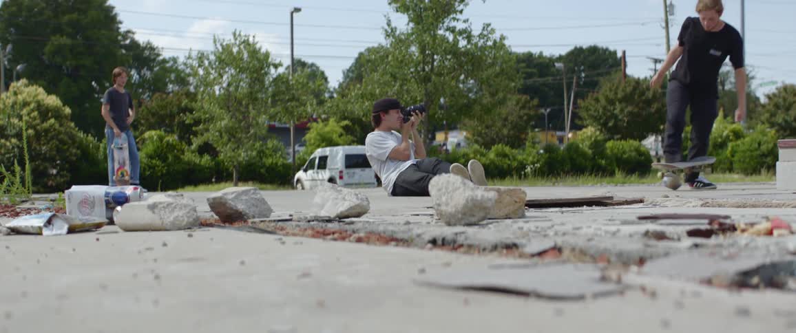 A teenager takes a photo of another teenager doing a skateboard trick