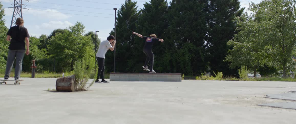 A young man on a skateboard performs a trick as one of his companions holds a camera to take pictures of the action