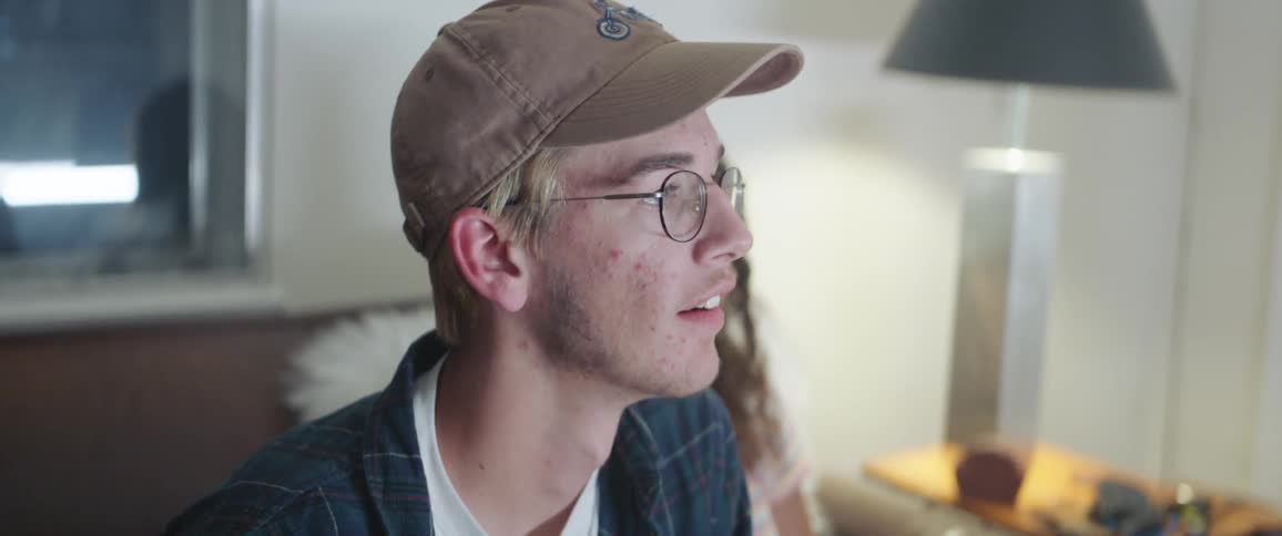 A young male sits on a couch with a female companion as he concentrates on playing a video game