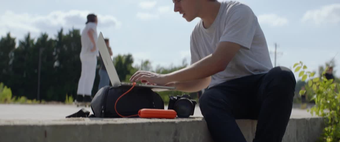 Teenager editing pictures on a laptop while sitting on a step outdoors