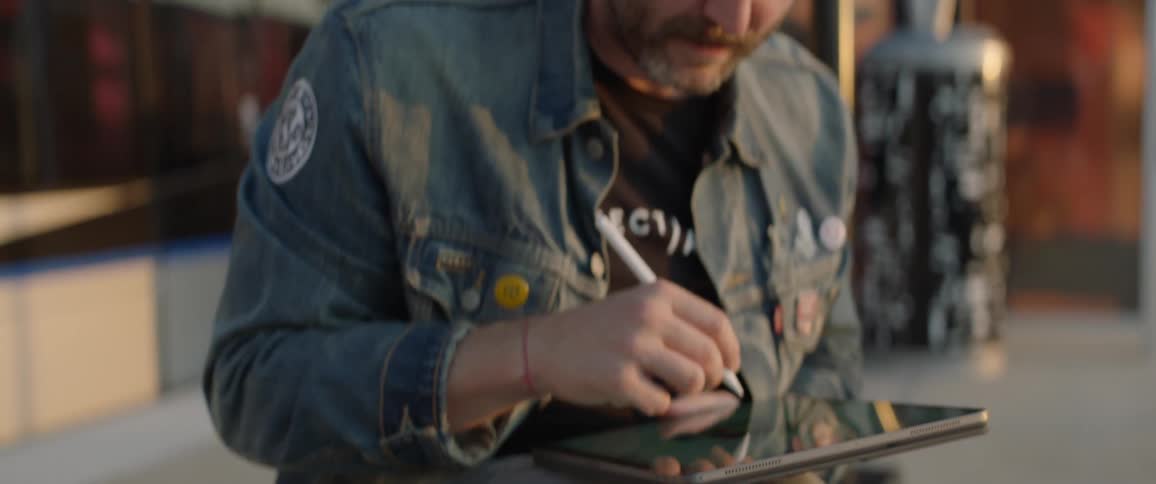 Man uses a digital pen on a tablet as a train travels behind him
